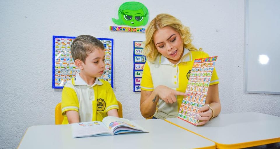 Profesora enseña un cartel de lectura a un alumno con su libro abierto