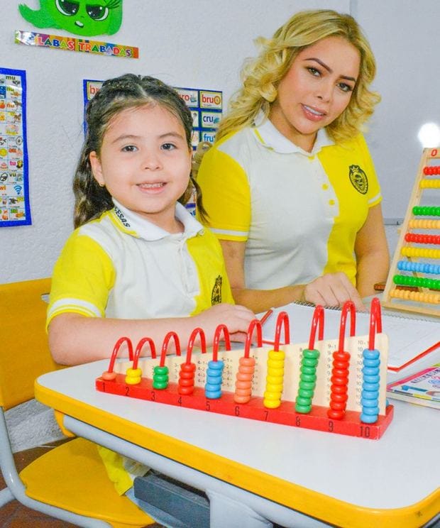 Alumna sonriente trabajando con un ábaco junto a su profesora en el aula